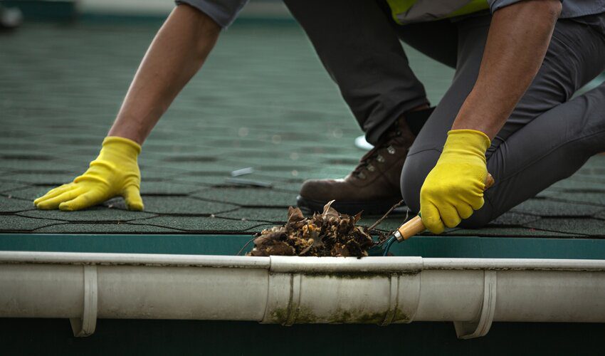 worker with yellow gloves standing on a roof cleaning gutters