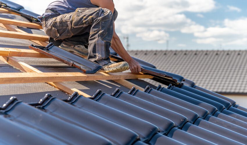 roofer installing ceramic tiles on a roof while sitting