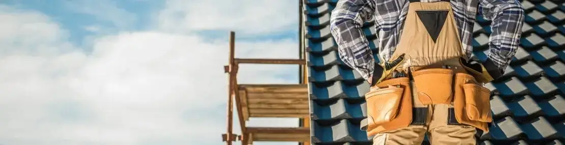 A back view of a man standing in front of a roof wearing a tool belt