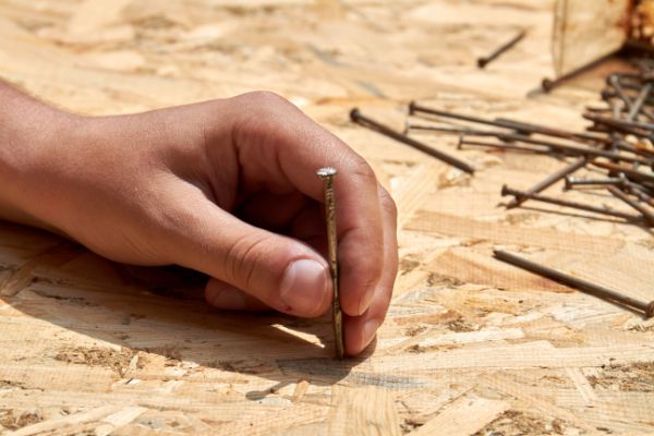 left hand holding a nail to a plywood